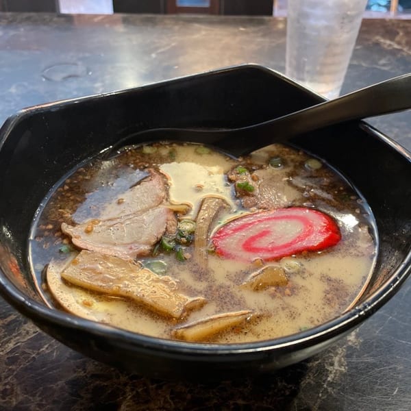 A close-up of a bowl of Daiichi Ramen with pork, bamboo shoots, and a pink swirl fish cake.