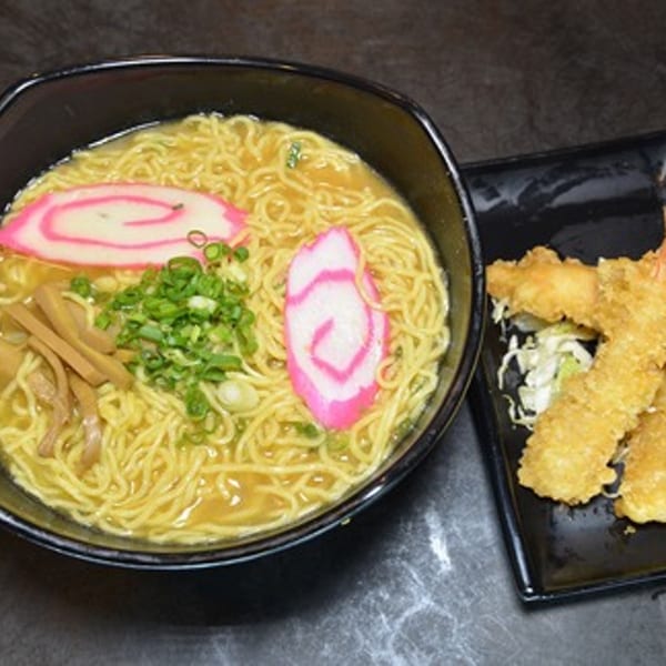 A bowl of Daiichi Ramen with fish cakes, green onions, and bamboo shoots, next to fried shrimp.